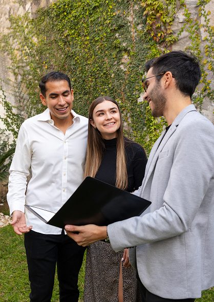 Agent reviewing documents with a smiling couple outdoors beside an ivy-covered wall
