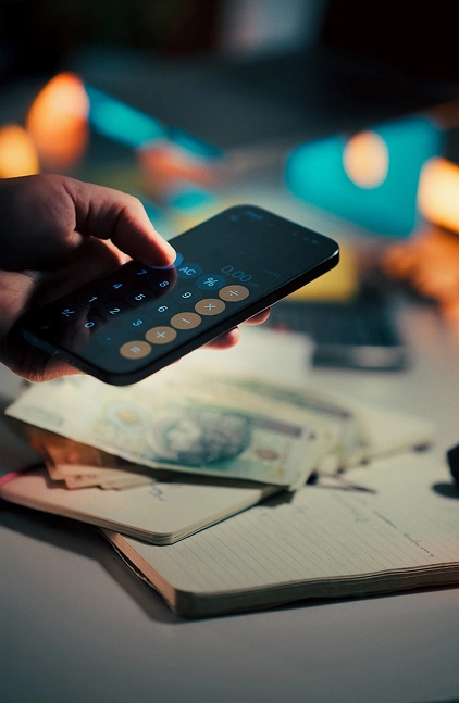 Hand using a smartphone calculator app above a desk with cash and an open notebook.