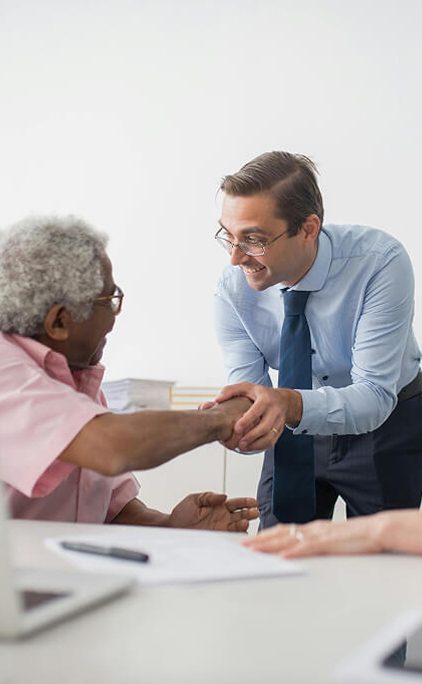Smiling financial advisor shaking hands with an older client across a desk after a retirement planning consultation.