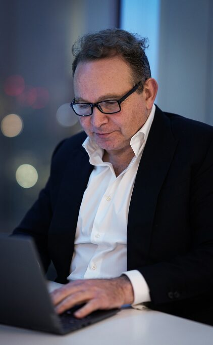 Financial advisor in a dark suit working on a laptop at a desk in an office at night.