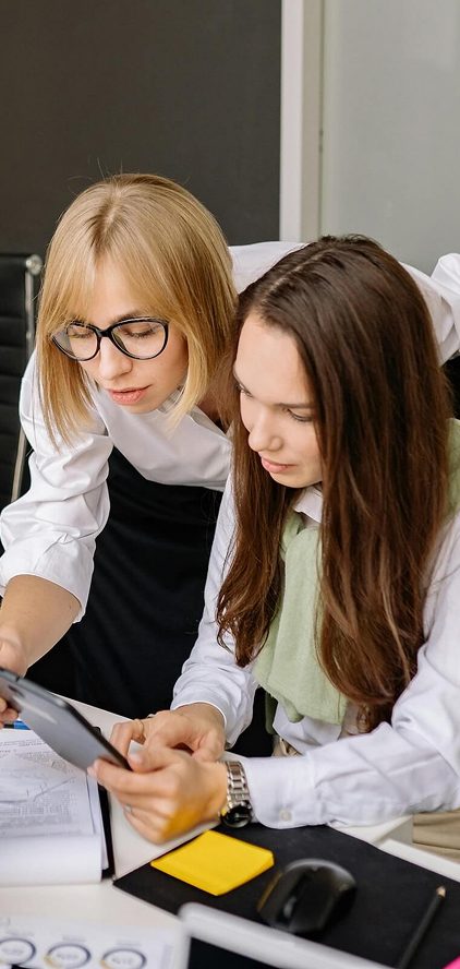 Two women in an office reviewing financial documents on a tablet together at a desk.
