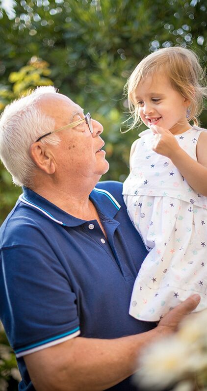 Grandfather holding his young granddaughter outdoors in a garden