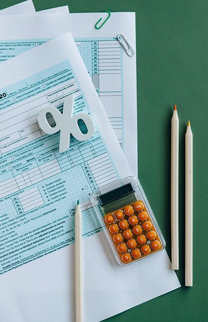 Flat lay of tax forms with a calculator, pencils, and a percentage symbol on a green background
