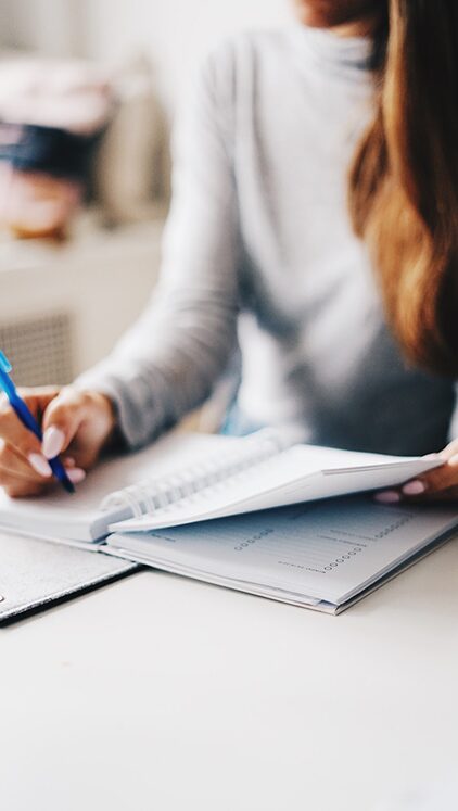 Woman writing retirement savings notes in a spiral notebook at a desk