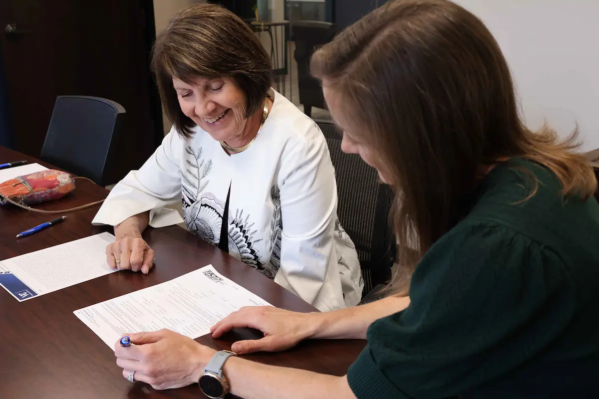 Smiling client reviewing a financial planning form with a financial advisor who guides her through it with a pen at a conference table.